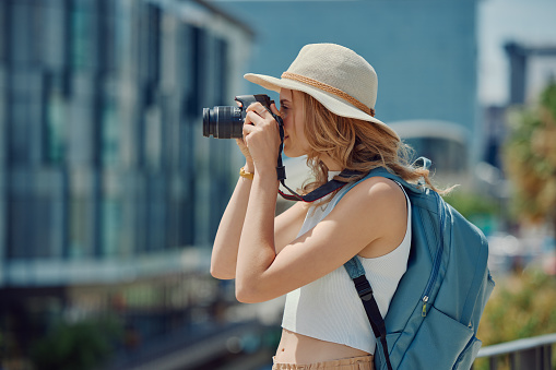 Camera, photography and woman in a city street for travel, holiday or vacation memory outdoor. Adventure, lens and profile of female photographer taking pictures of New York buildings for fun or tour