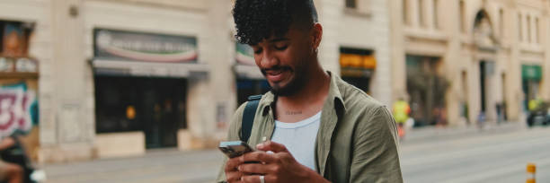istock Young smiling man with beard dressed in an olive color shirt uses phone map app on the old city background, Panorama 1967540663