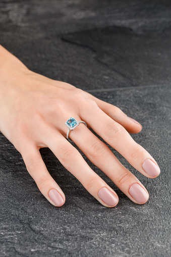 Beautiful female hand with gold ring with diamonds and aquamarine on gray background close-up