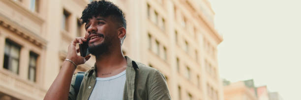 istock Young happy man with beard dressed in an olive-colored shirt is talking on cellphone standing on the old city background, Panorama 1967541405