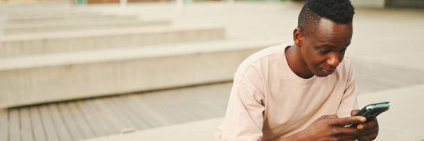 istock Young african student sits outside of university, uses cellphone, taps on smartphone screen, Panorama 1967543448