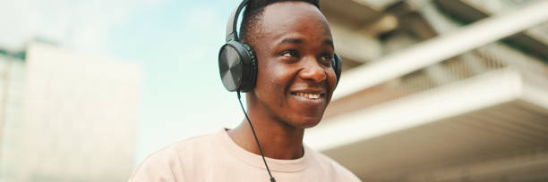 istock Young african student sitting outside of university and taking notes while study online with headphones, Panorama 1967548034