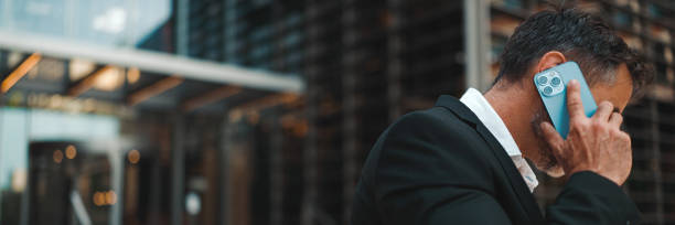 istock Middle-aged businessman with neat beard in office clothes uses mobile phone, Panorama. Successful man emotionally talking on smartphone. Disappointment, trouble 1967549169