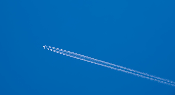 A distant airplane, aeroplane leaving a vapour trail from its four jet engines far up in a deep blue sky