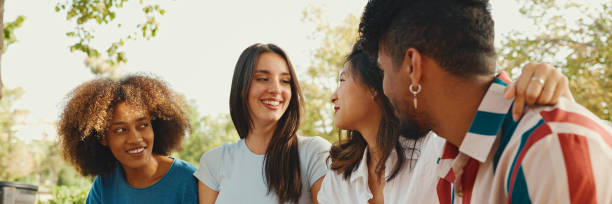 istock Happy multiethnic young people talking while sitting on park bench on summer day outdoors, Panorama. Group of friends talking and laughing merrily in city park 1967573528