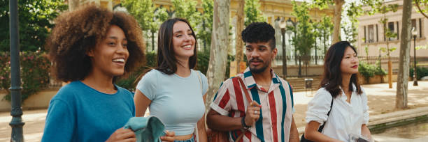 istock Happy multiethnic young people walk embracing on summer day outdoors, Panorama. Group of friends are talking and laughing merrily while walking along on the street 1967578368