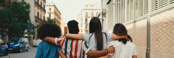 istock Happy multiethnic young people walk embracing on summer day outdoors, Back view, Panorama. Group of friends are talking and laughing merrily while walking along on the street 1967585283