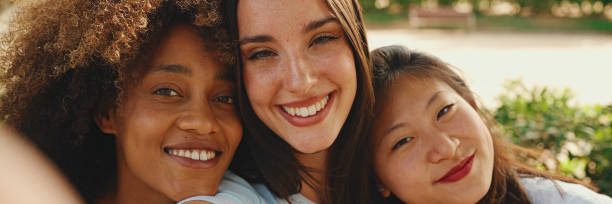 istock Happy, lovely multiethnic young women posing on cellphone camera on summer day outdoors. group of friends hugging each other smiling at the camera while standing on path in the park 1967586351