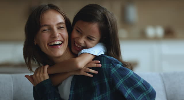 Joyful cute girl embracing happy young mom from behind