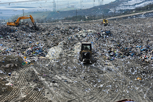 A bulldozer pushing waste at a landfill, with many birds and a panoramic view in the distance.