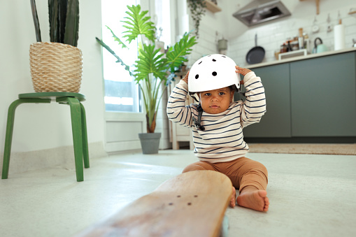 Cute little baby boy playing with protective helmet and skateboard at home