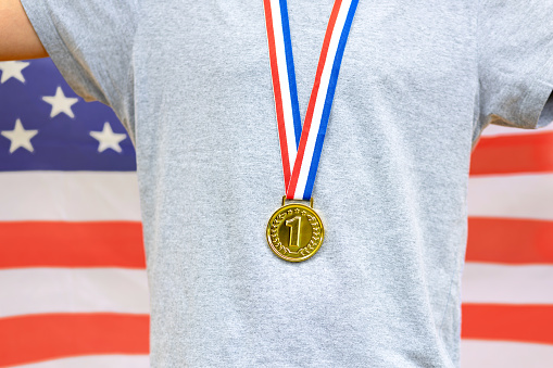 Triumphant american male athlete proudly displays a gold medal, symbolizing victory. The United States flag on his back represents national pride during sporting events