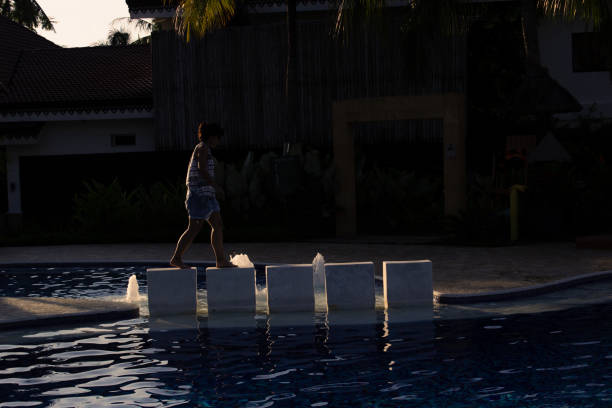 Beautiful woman in a swimming pool in the Philippines, walking on top of some white stone blocks, balancing.