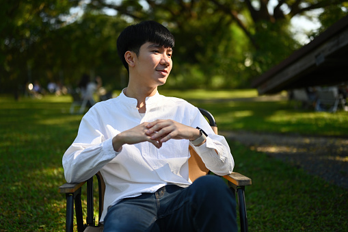 Portrait of a smiling handsome young Asian man sitting the outdoors in the morning with a sunkissed face.