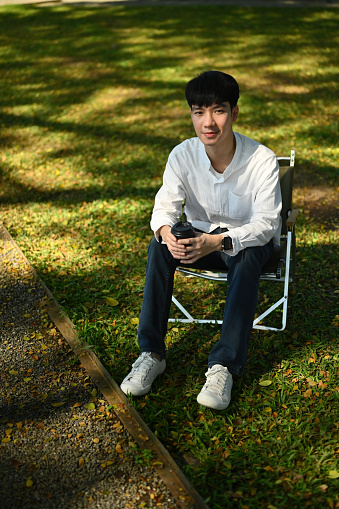 High-angle view and Full-length portrait of a Young Asian man sitting on a lawn chair, outdoors in the morning with a sunkissed face.
