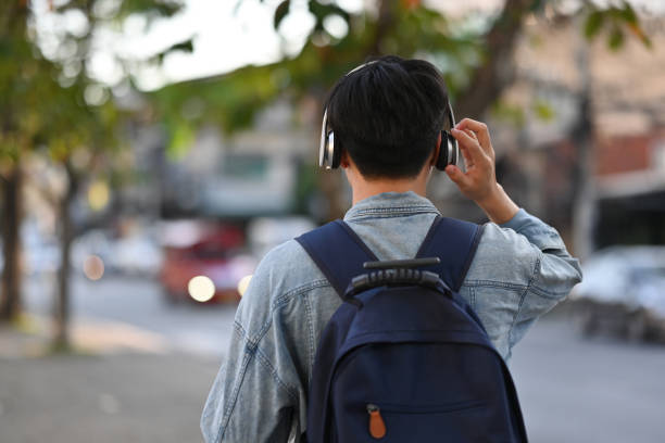 Rear view of Asian backpacker male walking on footpath while listening a music from headphones in the urban city, Solo travel concept Rear view of Asian backpacker male walking on footpath while listening a music from headphones in the urban city, Solo travel concept. asian man headphones stock pictures, royalty-free photos & images