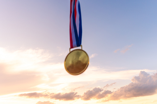 Blurred gold medal symbolizing triumph on the podium against a golden sky adorned with sunset clouds. It represents the pursuit of victory and first place in sporting events