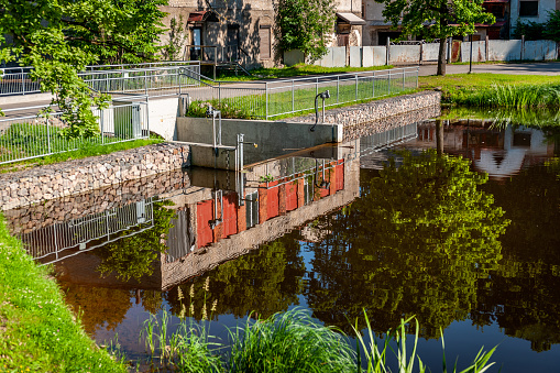 Old dam on the pond. Concrete construction with reflection in water. Sunny summer day. Gateway with water.