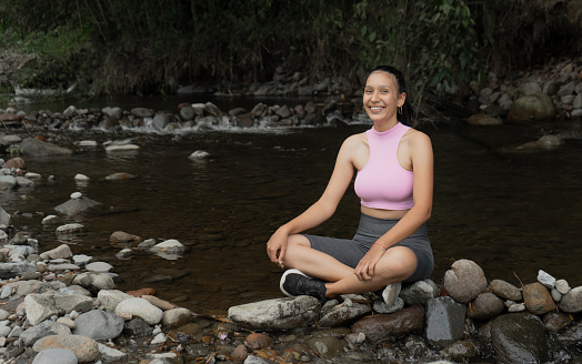 portrait of young woman sitting in comfortable clothes by the river bank and smiling happily