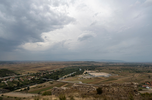 A landscape photograph of a storm that hangs over the industrial part of the City of Niš. Observed from the locality Korvin Grad, which is located near the town of Nis. Panoramic photo.