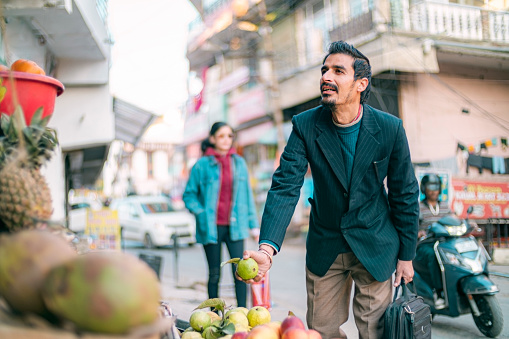 A pedestrian man shops at a greengrocer's street shop while commuting after work in the 15-minute city of Himachal Pradesh.