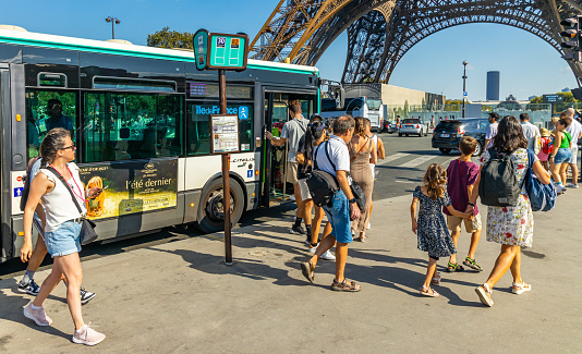 Paris, France - September 09, 2023 : RATP bus parked in front of the Eiffel Tower on a sunny day in Paris, France with tourists getting out if the autocar