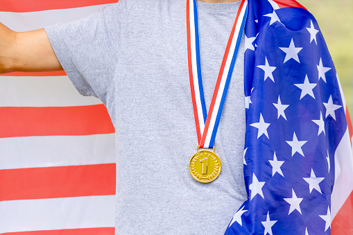 Triumphant american male athlete proudly displays a gold medal, symbolizing victory. The United States flag on his back represents national pride during sporting events