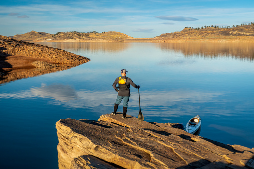 male canoe paddler with a paddle on  a rocky shore of a mountain lake - Horsetooth Reservoir in northern Colorado in fall or winter scenery