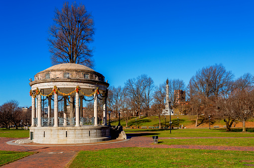 Boston, Massachusetts, USA - January 12, 2024: The Parkman Bandstand is a landmark bandstand located on the eastern side of the Boston Common in Boston. It was built in 1912. In 1996, the bandstand was restored and is used today for concerts, rallies, and speeches. The Boston Common (also known as the Common) is a central public park in downtown Boston, Massachusetts. Dating from 1634, it is the oldest city park in the United States. The Soldiers and Sailors Monument is in the background.