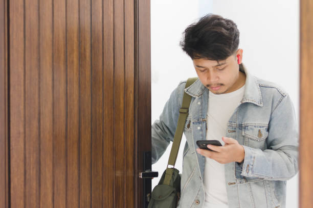 istock A young Asian man wearing a t-shirt and jeans jacket leaving the house while using a cellphone and earpiece 1967904545
