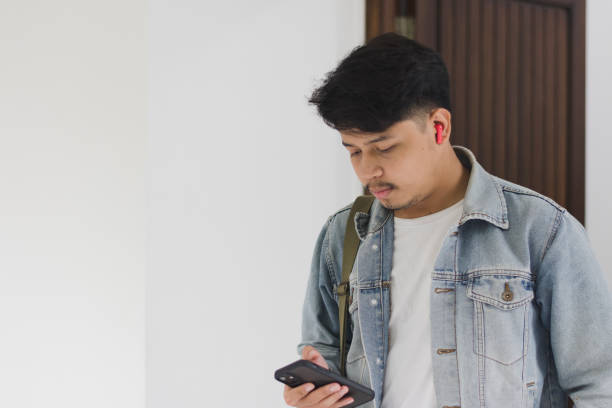 istock A young Asian man wearing a t-shirt and jeans jacket leaving the house while using a cellphone and earpiece 1967908741