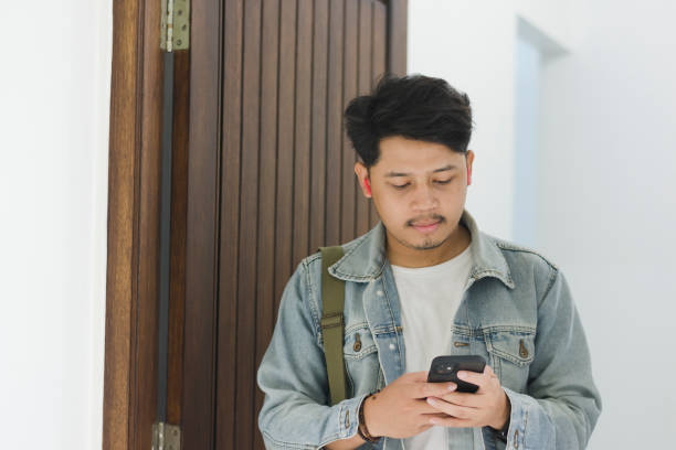 istock A young Asian man wearing a t-shirt and jeans jacket leaving the house while using a cellphone and earpiece 1967908743