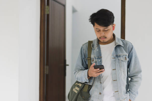 istock A young Asian man wearing a t-shirt and jeans jacket leaving the house while using a cellphone and earpiece 1967908744