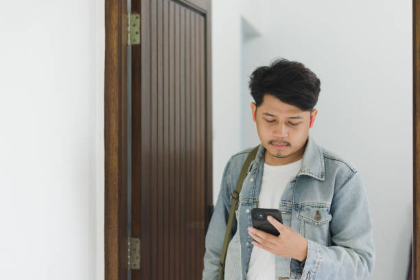 istock A young Asian man wearing a t-shirt and jeans jacket leaving the house while using a cellphone and earpiece 1967908745