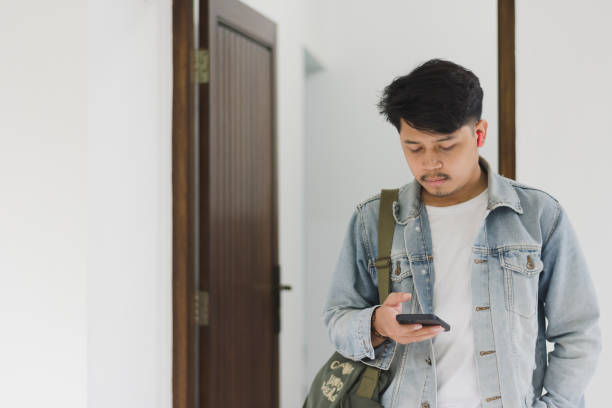 istock A young Asian man wearing a t-shirt and jeans jacket leaving the house while using a cellphone and earpiece 1967911917