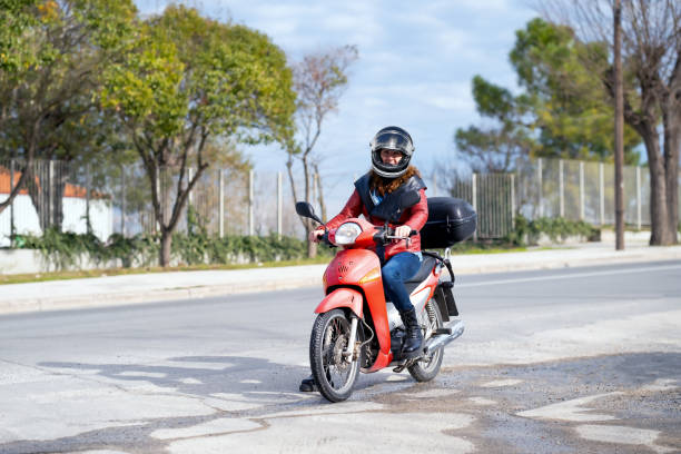 Woman biker riding her red motorcycle against a buildings and trees
