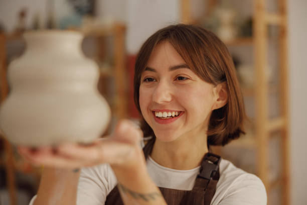 istock Smiling female potter wearing apron holding unfired clay vase while standing in pottery studio 1967937855