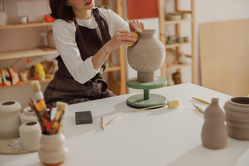 Close up of female ceramist work with unfired clay vase in pottery studio. High quality photo