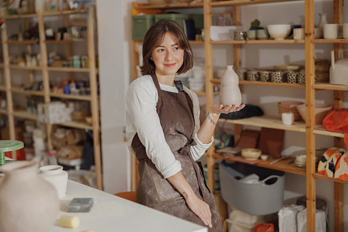 Smiling entrepreneur crafts woman holding mug in pottery studio while looks away