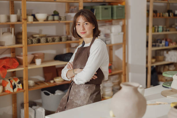 istock Portrait of young female potter in apron looking at camera while posing in workshop 1967950736