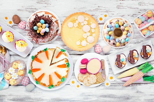 Easter or spring dessert food table scene. Overhead view on a white wood background. Lemon tart, cupcakes, Easter egg and carrot cakes and a selection of sweets.