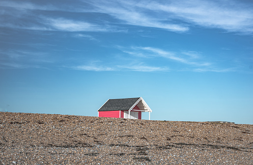 Single little cabin hiding behind pebble dune on a beach of Lancin, West Sussex, UK