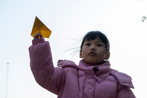 Low angle photography of little Asian girl playing with paper airplane