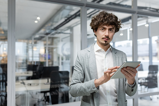 Portrait of serious mature businessman, thinking man with tablet computer in hands looking at camera, worker entrepreneur at workplace in business suit.