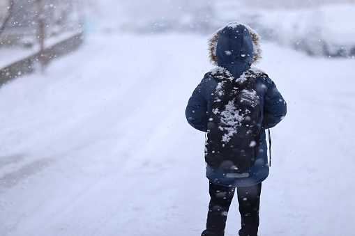 Front view of unhappy and sad small child standing in snow, holiday in winter nature.