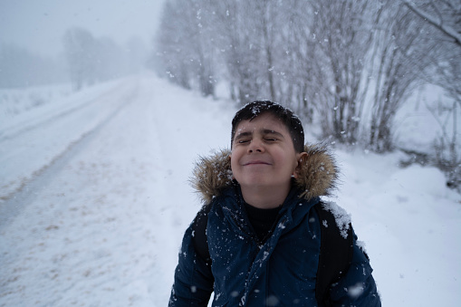 Happy kid boy with having fun with snow on way to school