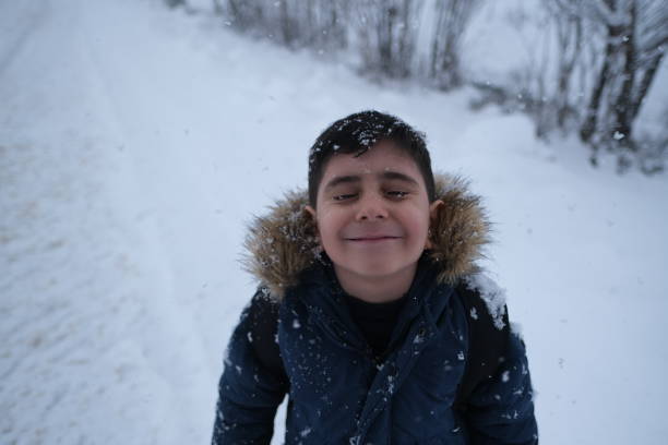 Happy kid boy with having fun with snow on way to school