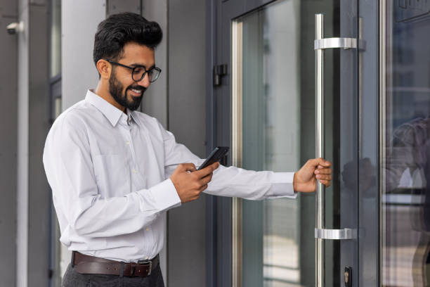 Smiling professional man in glasses using smartphone while entering modern office building