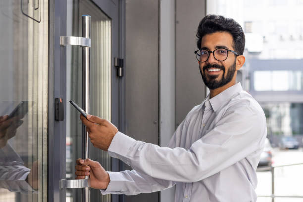 istock Confident young businessman with glasses smiling while entering modern office building using smartphone 1968124154