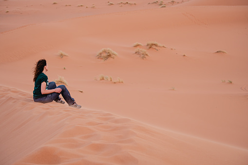 Young woman sitting on sand dunes in the Sahara desert, Morocco